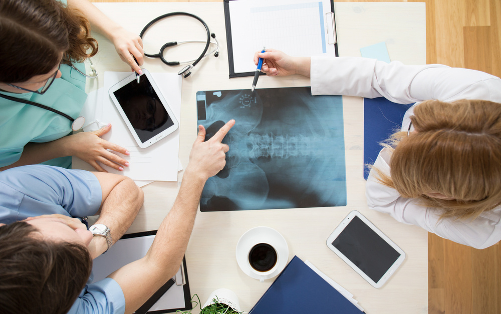 Doctors sitting around the table and interpreting x-ray image Doctors sitting around the table and interpreting x-ray image